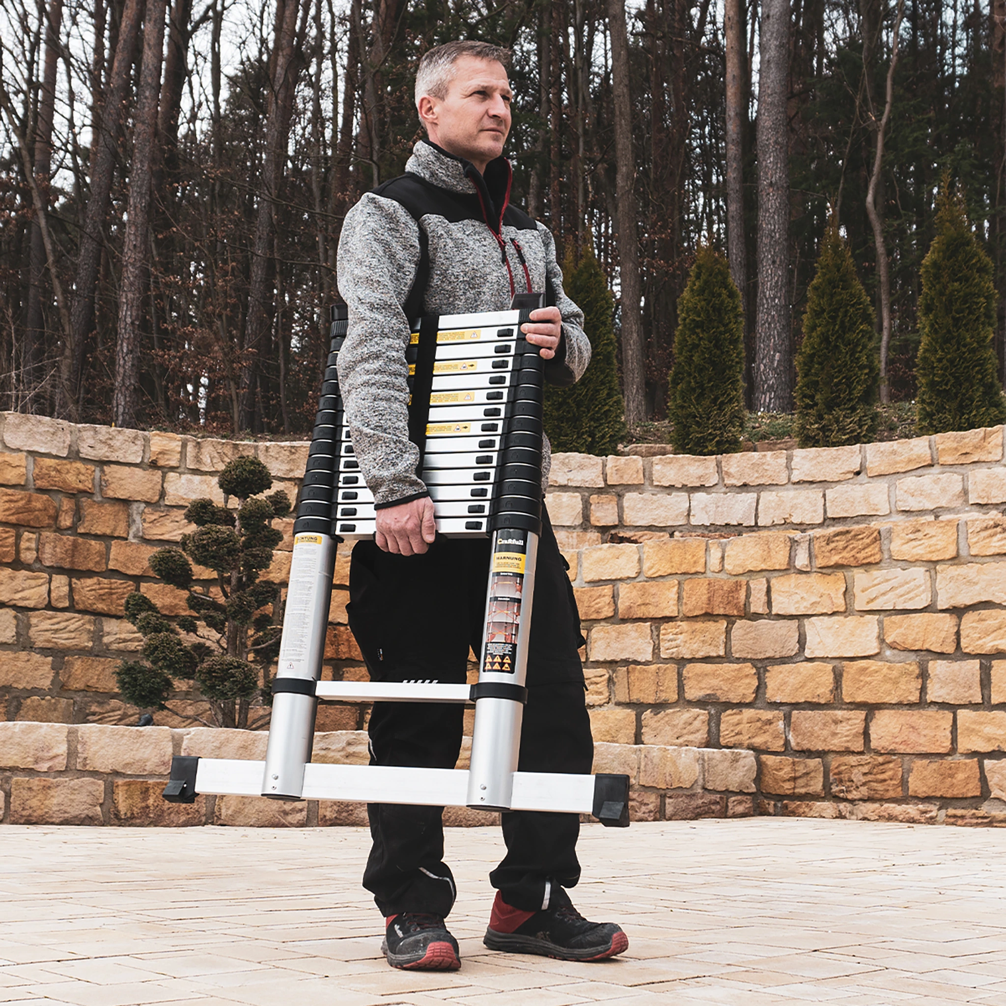 Lange Garantie von drei Jahren Heimwerker trägt zusammengeklappte Teleskopleiter unter dem Arm