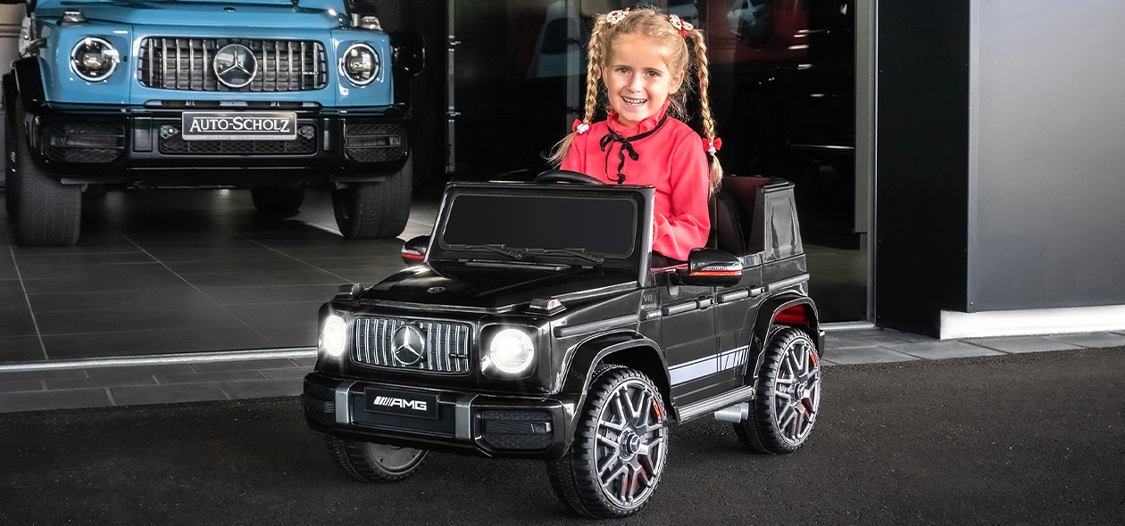 Actionbikes Kinder-Elektroauto Mercedes AMG G63 W463 Mädchen sitzt lächelnd im Kinder-Elektroauto Mercedes AMG G63 W463