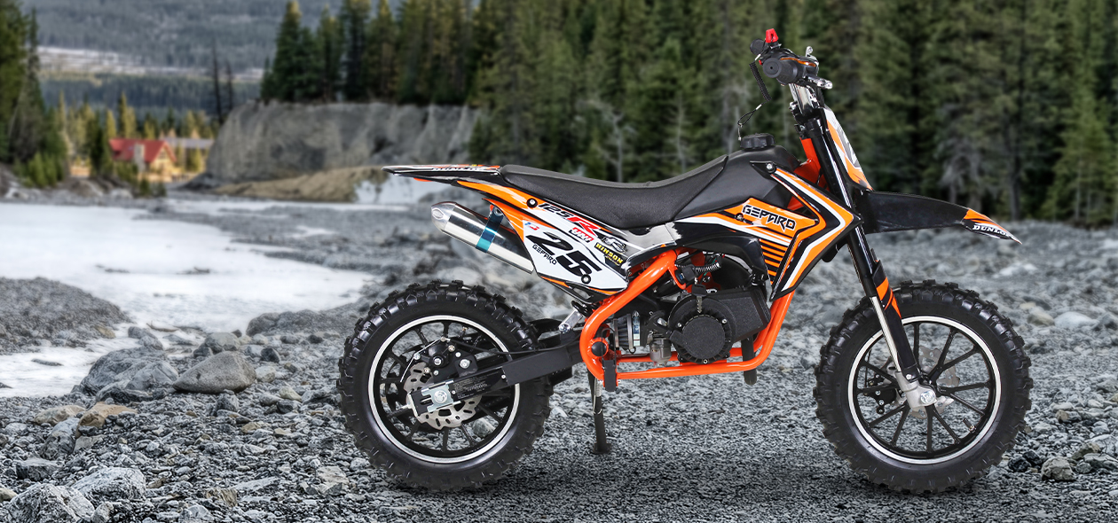 Kinder-Motocross-Bikes in Orange auf felsigem Untergrund vor einem Wald