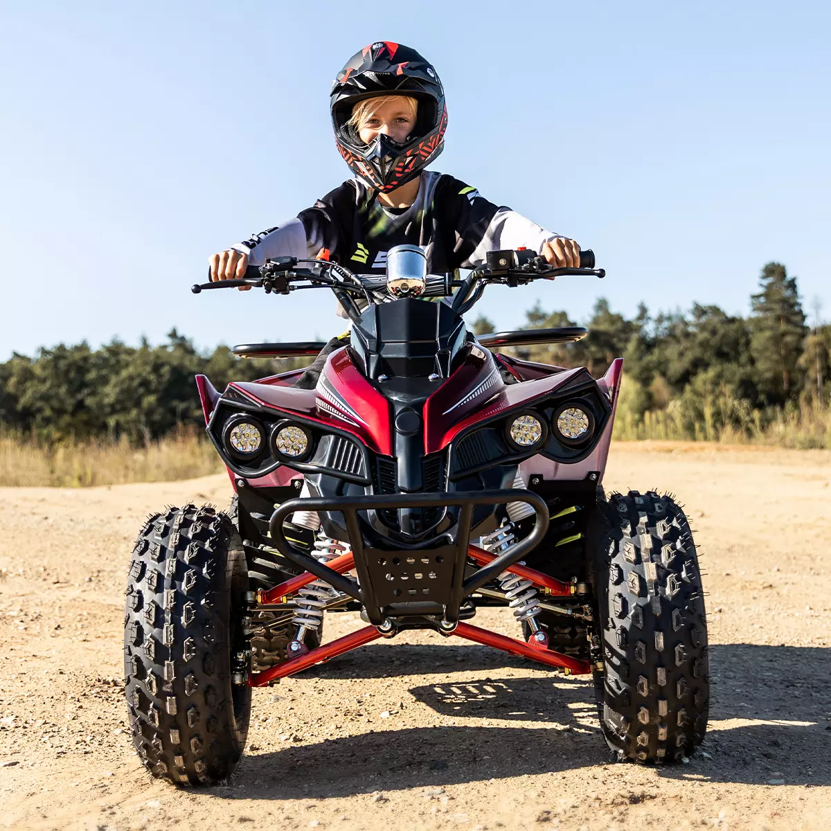 Junge mit Helm steuert das Benzin-Kinderquad über sandigen Untergrund