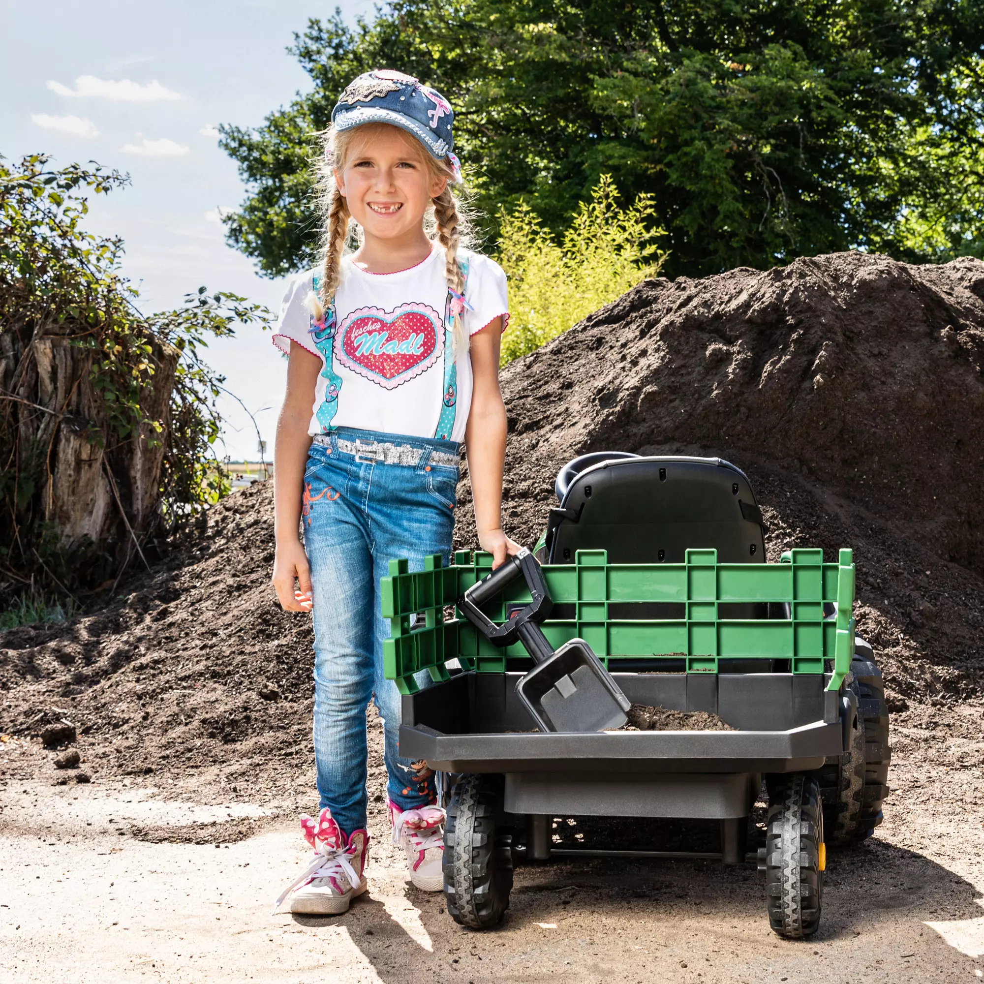 Mädchen stützt sich am Anhänger des Elektro-Kindertraktors ab