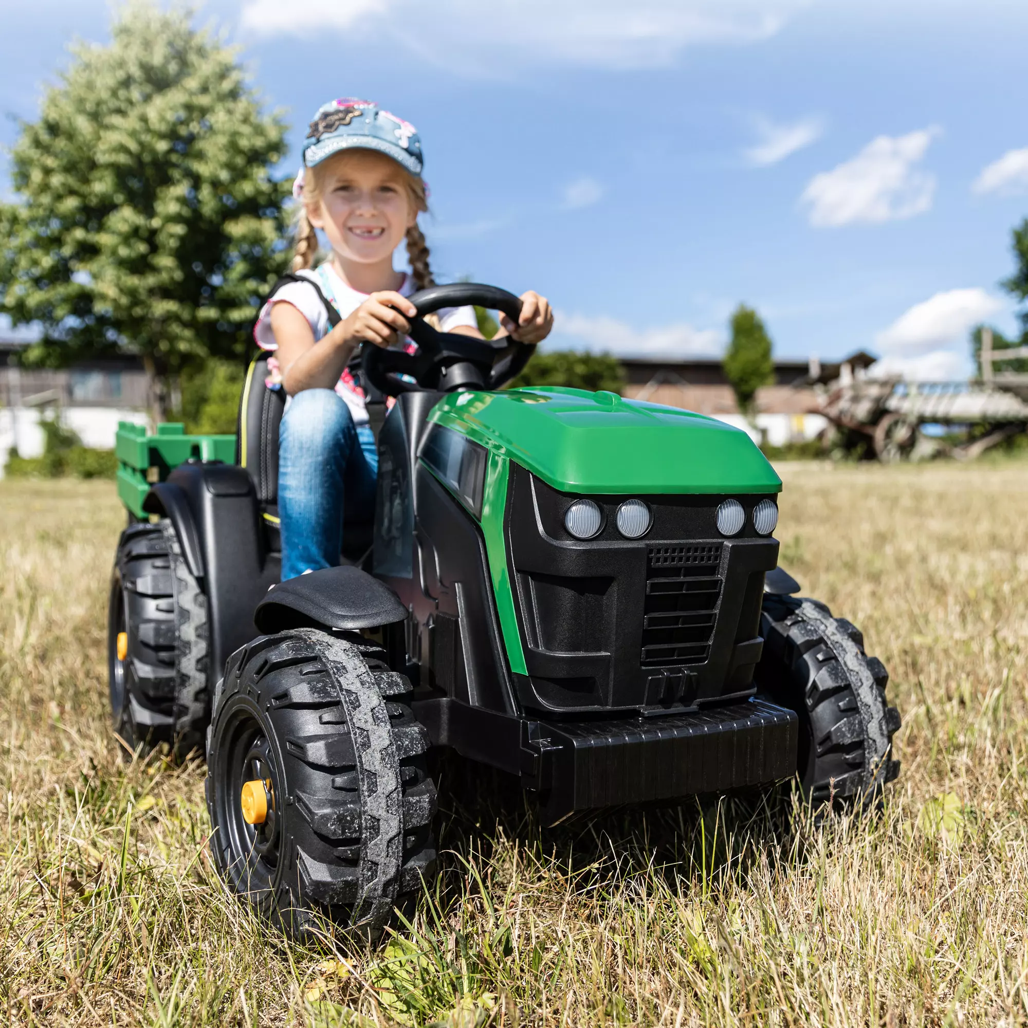 Mädchen steuert den Kindertraktor in Schwarz und Grün über eine Wiese