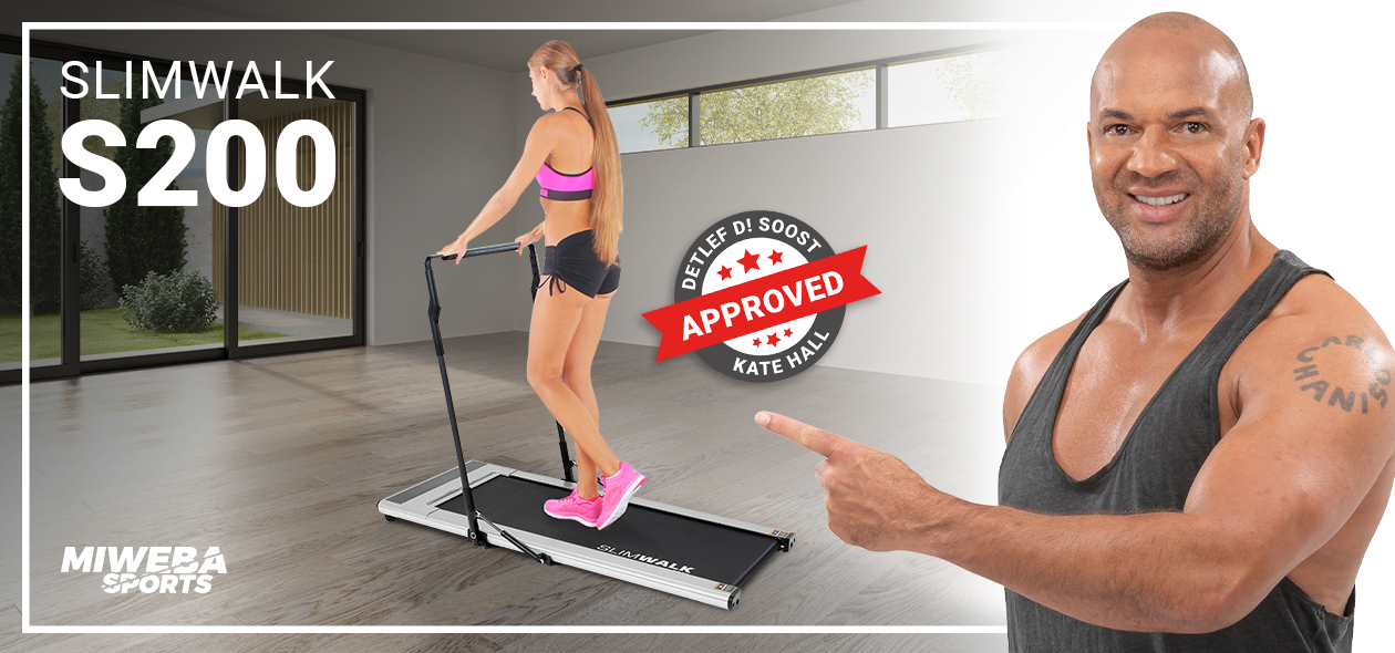 Miweba Sports Laufband SlimWalk S200 Detlef D! Soost zeigt lächelnd auf eine Frau, die auf einem Laufband trainiert