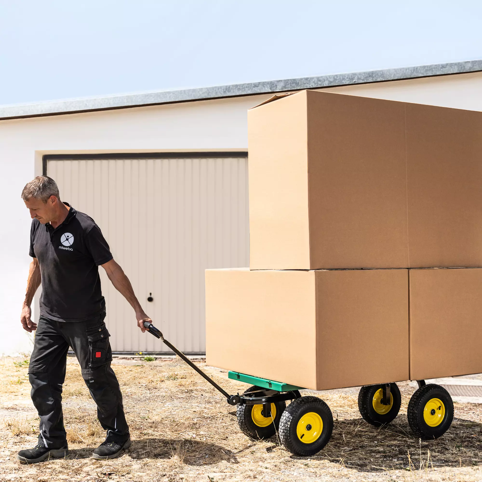 Hohe Traglast bis 700 kg Ein Mann transportiert große Kartons auf der Ladefläche des Bollerwagens im Hof