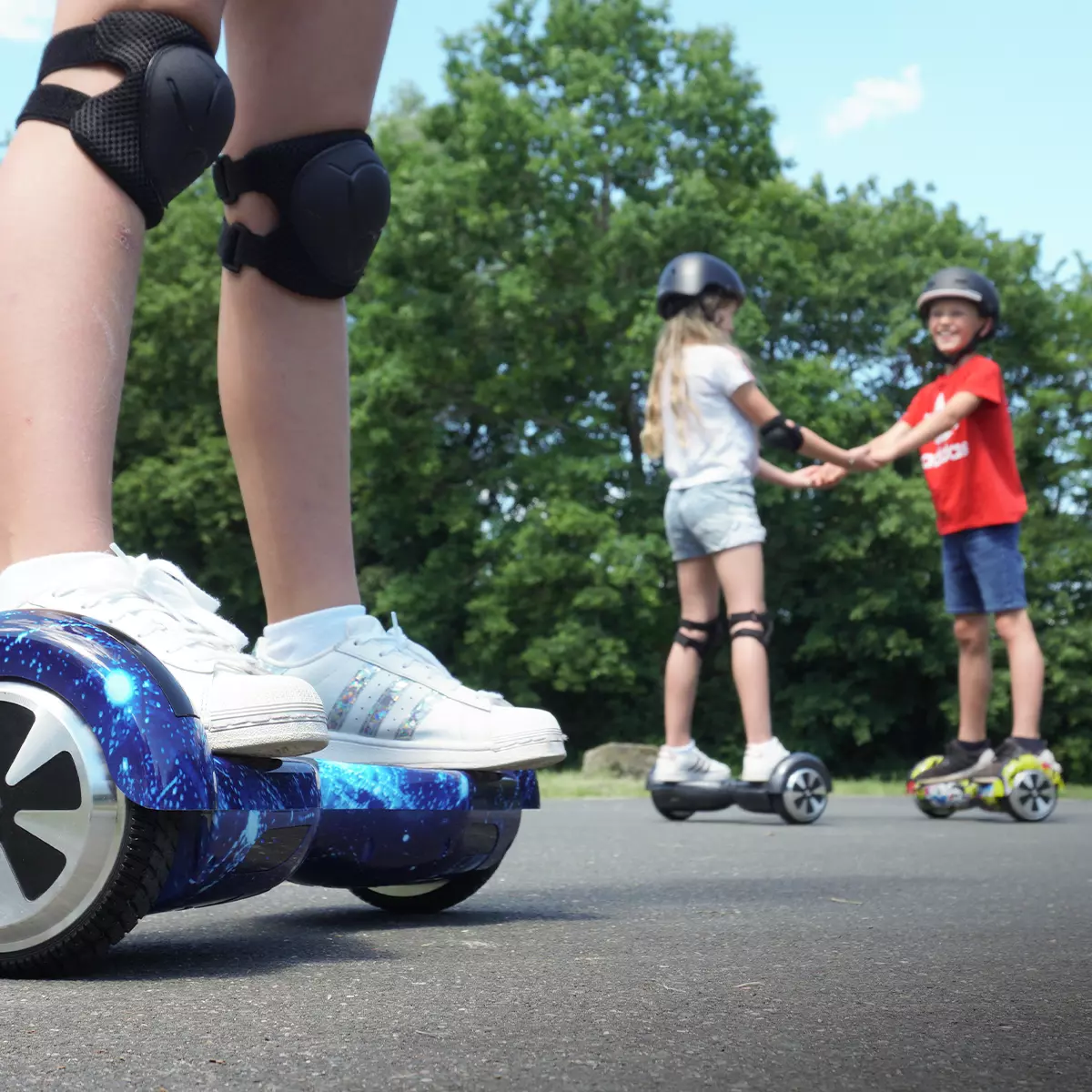 Füße eines Kindes auf Hoverboard, zwei Kids halten sich an Händen und stehen auf je einem Hoverboard