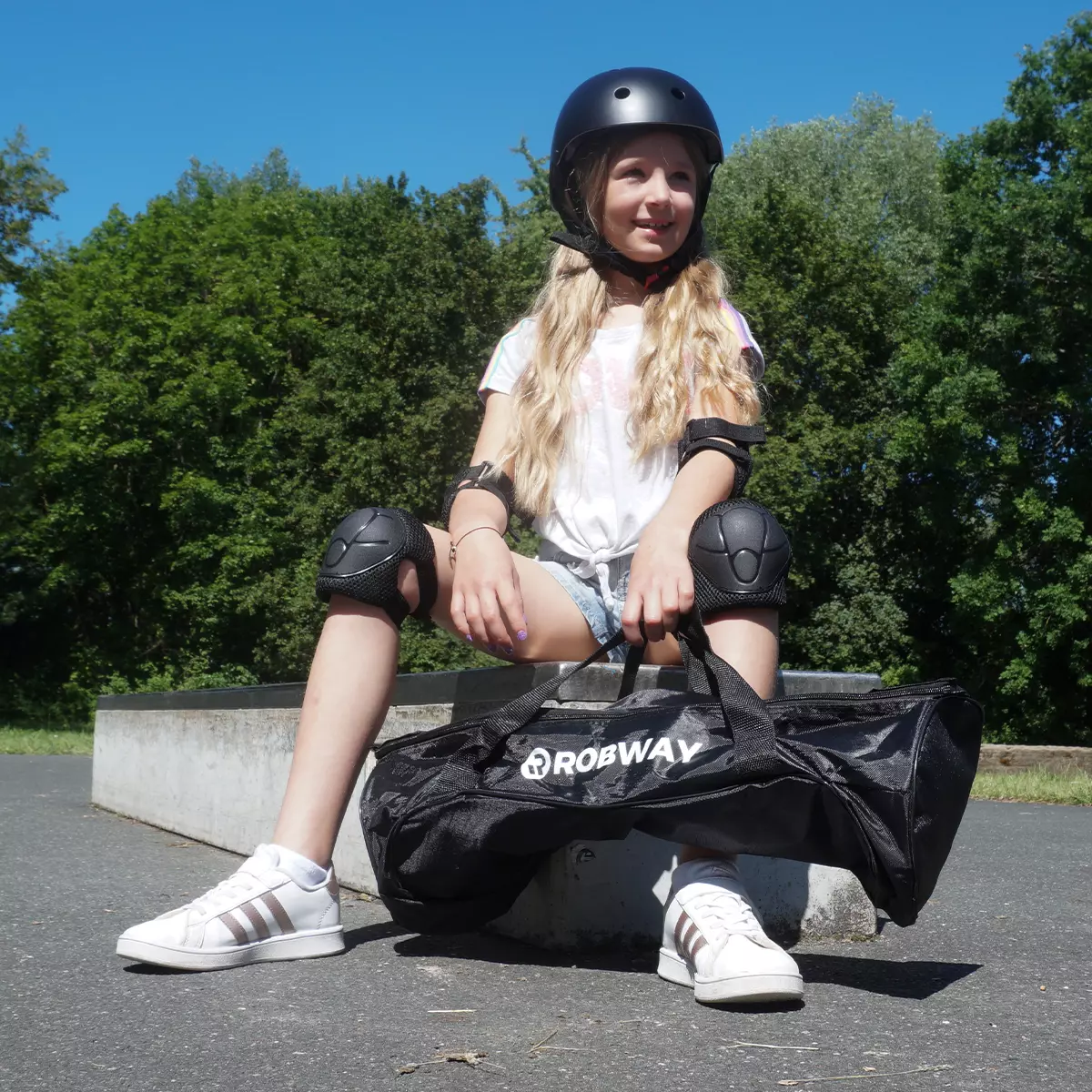 Mädchen sitzt auf Bank im Park und hält Tasche mit dem Hoverboard in der Hand